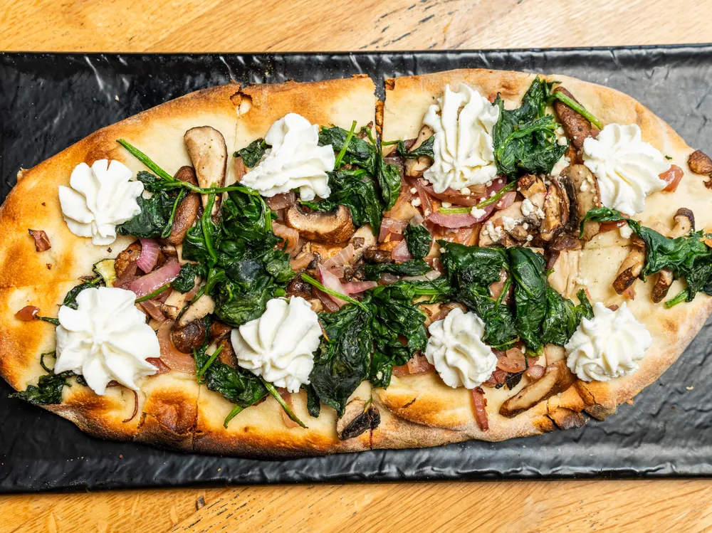 A flatbread with spinach, mushrooms and dollops of soft cheese on a slate board
