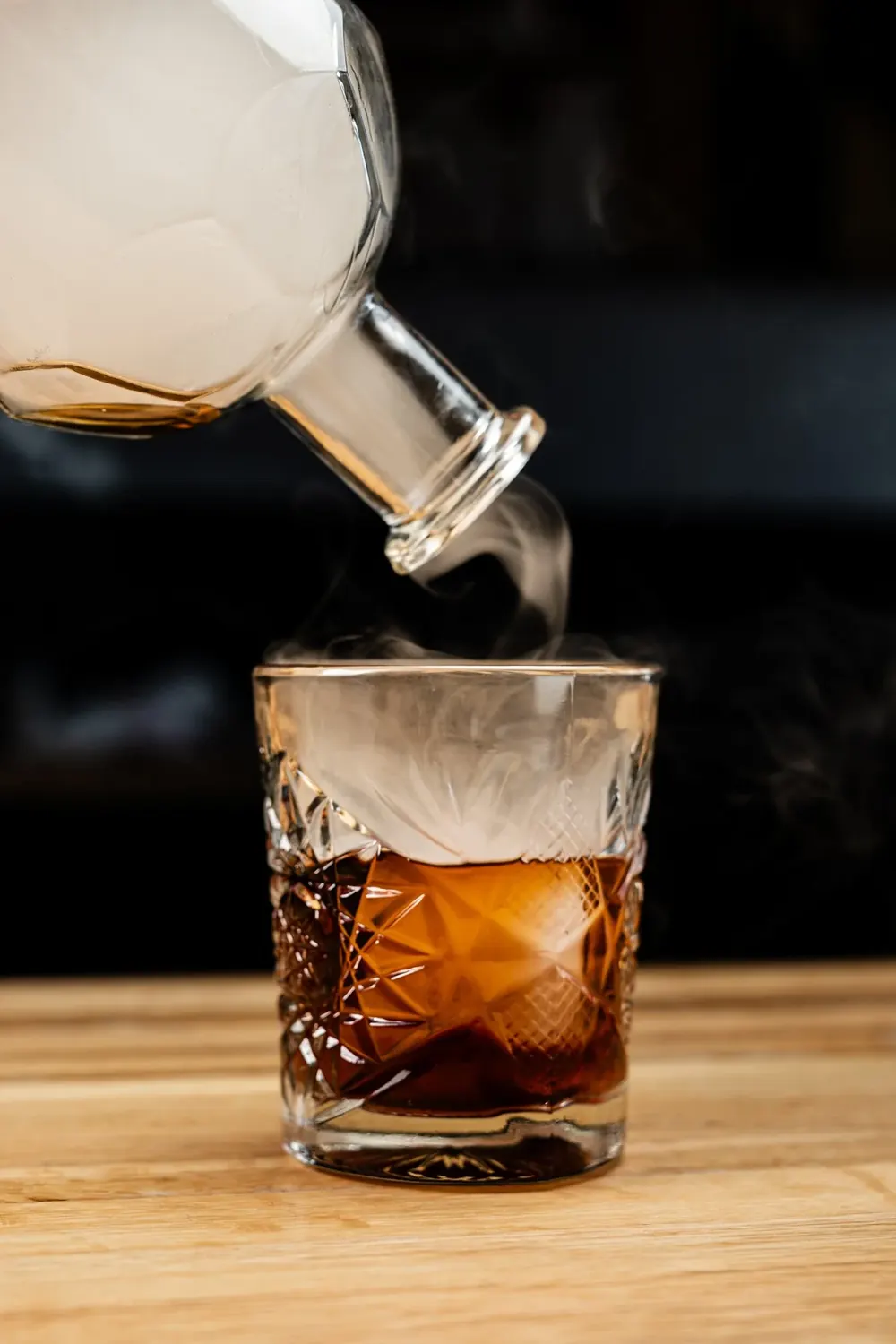 Whiskey poured from a decanter into a cut glass over a large cube