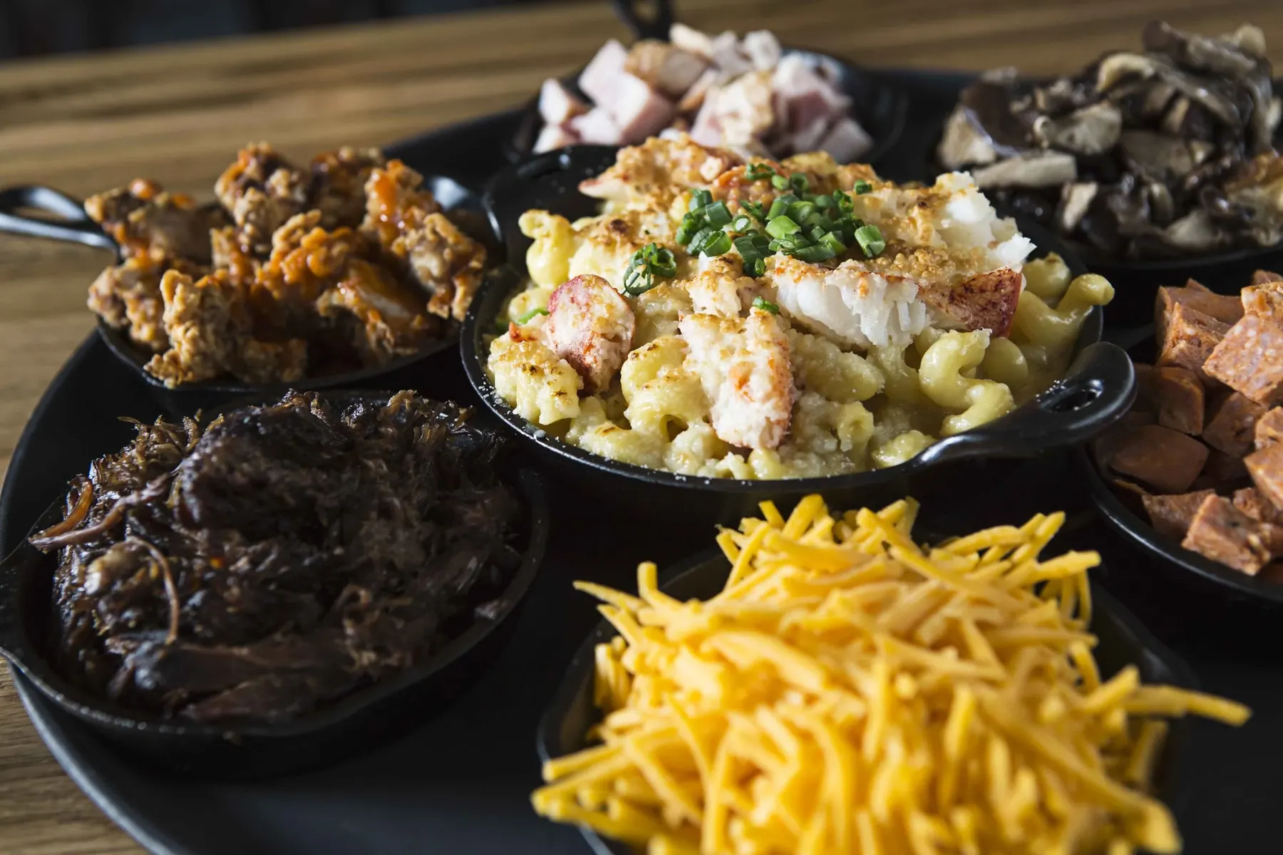 Cast iron dishes of mac and cheese with toppings: lobster, pork, mushrooms and shredded cheddar