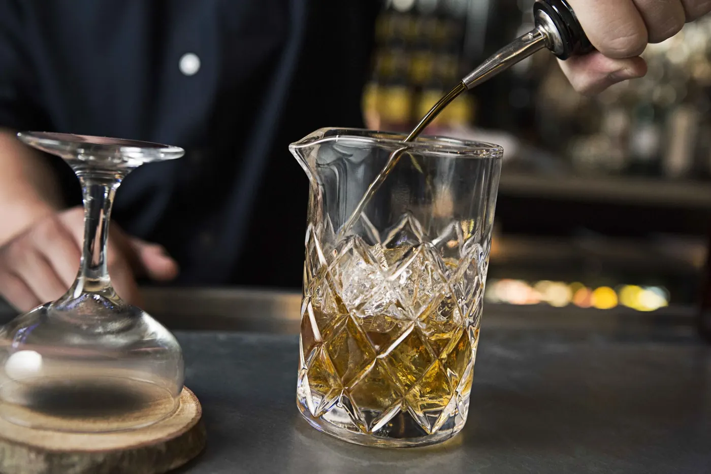 A bartender stirring a drink in a cut glass mixing tin