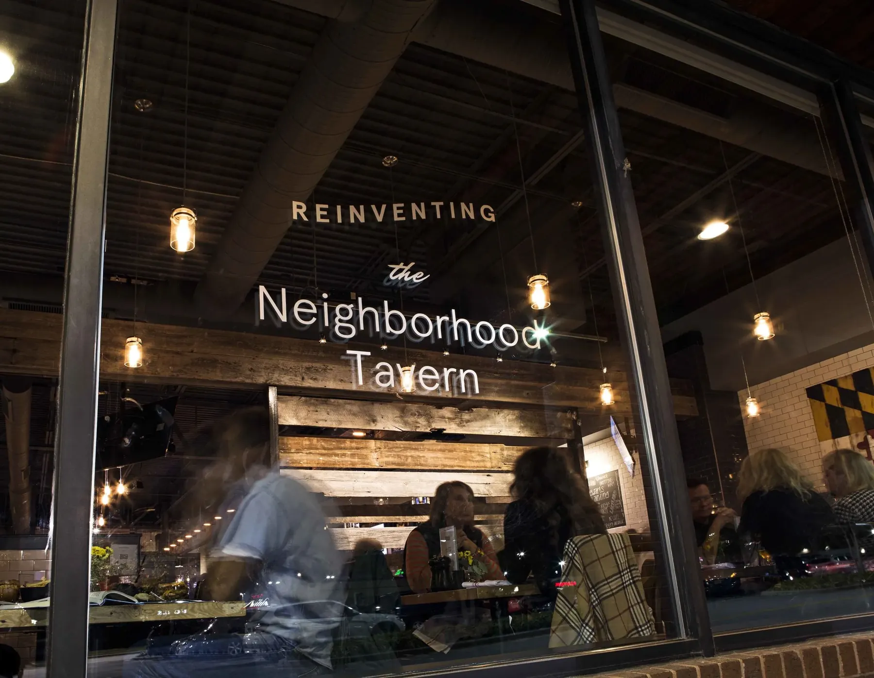 The front window at night, lettered Reinventing the Neighborhood Tavern